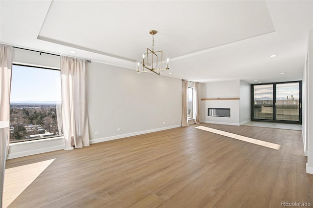 unfurnished living room with a tray ceiling, a chandelier, and light hardwood / wood-style floors