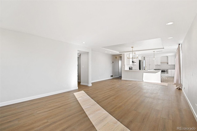 unfurnished living room with a tray ceiling, a chandelier, and light wood-type flooring