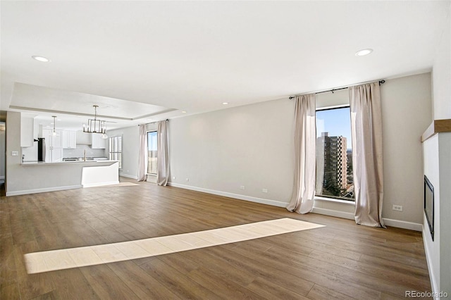 unfurnished living room with hardwood / wood-style floors, a notable chandelier, a raised ceiling, and sink