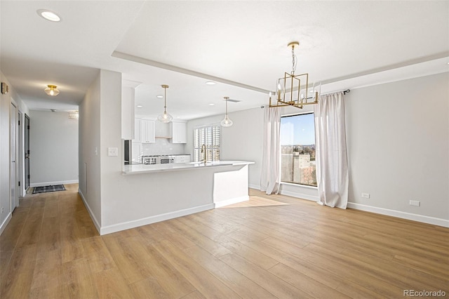 kitchen featuring white cabinetry, sink, hanging light fixtures, kitchen peninsula, and a chandelier