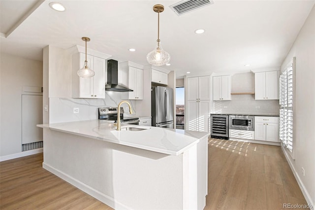 kitchen with white cabinetry, wall chimney exhaust hood, hanging light fixtures, kitchen peninsula, and appliances with stainless steel finishes