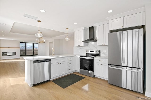 kitchen with white cabinets, wall chimney exhaust hood, appliances with stainless steel finishes, decorative light fixtures, and kitchen peninsula