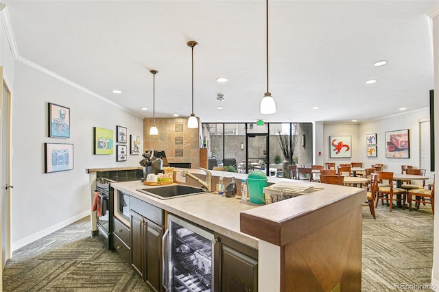 kitchen with dark brown cabinetry, a kitchen island with sink, sink, wine cooler, and hanging light fixtures