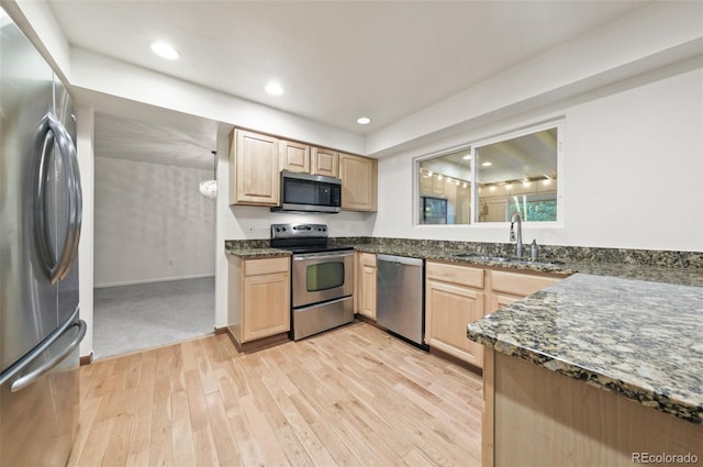 kitchen featuring light brown cabinetry, light wood-type flooring, dark stone counters, stainless steel appliances, and sink