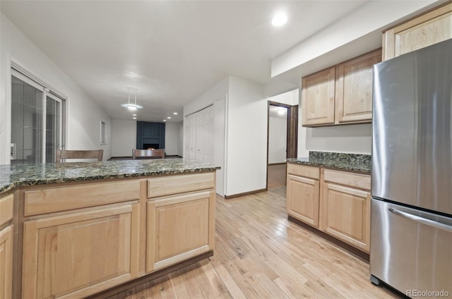 kitchen with light brown cabinetry, light hardwood / wood-style floors, stainless steel refrigerator, and dark stone counters