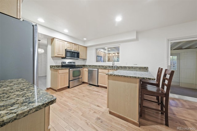 kitchen with sink, light hardwood / wood-style flooring, kitchen peninsula, a breakfast bar area, and appliances with stainless steel finishes