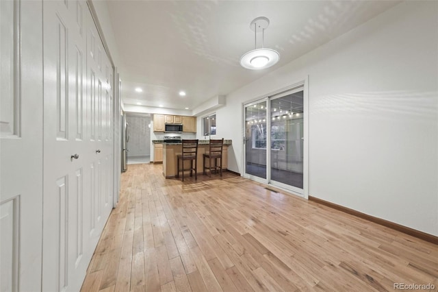 kitchen with a kitchen breakfast bar, stainless steel appliances, light hardwood / wood-style flooring, and hanging light fixtures