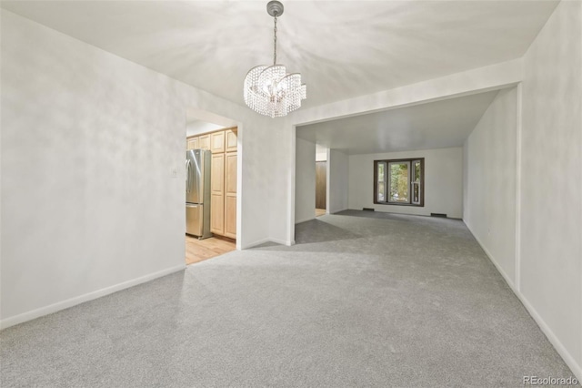 empty room with light colored carpet and an inviting chandelier