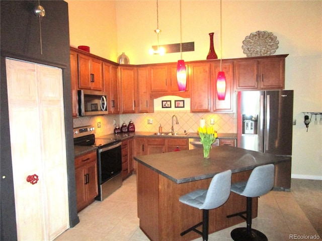 kitchen with dark countertops, a kitchen island, appliances with stainless steel finishes, pendant lighting, and a sink