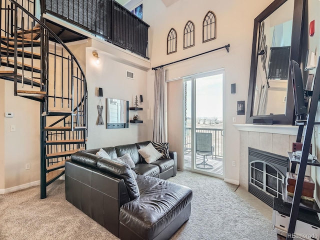 carpeted living area featuring visible vents, stairway, baseboards, a towering ceiling, and a tile fireplace