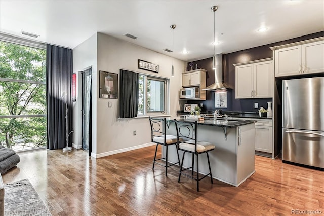 2958 Syracuse St Unit 214, Denver, CO 80238 - kitchen with a kitchen breakfast bar, visible vents, baseboards, stainless steel appliances, and wall chimney exhaust hood