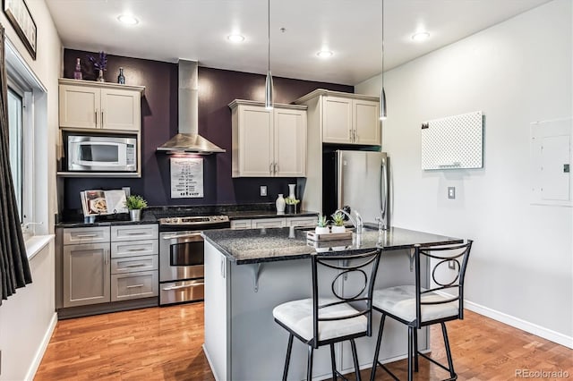 2958 Syracuse St Unit 214, Denver, CO 80238 - kitchen with wall chimney range hood, a breakfast bar area, appliances with stainless steel finishes, a center island with sink, and light wood-style floors