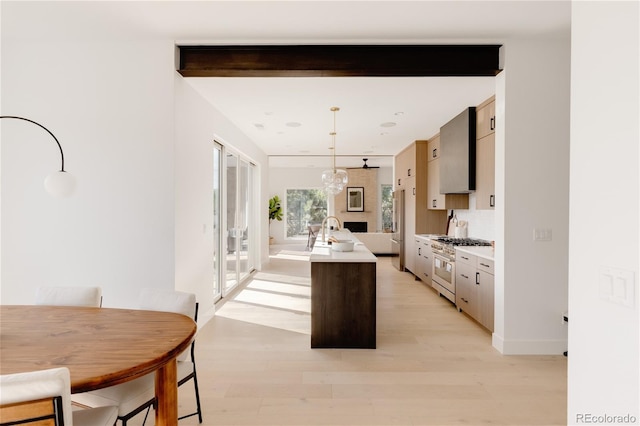 kitchen with light wood-type flooring, pendant lighting, beamed ceiling, stainless steel range, and a center island with sink