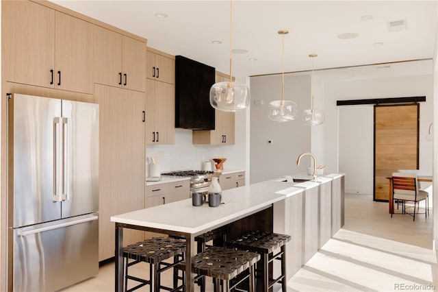 kitchen featuring light brown cabinetry, range hood, appliances with stainless steel finishes, hanging light fixtures, and sink