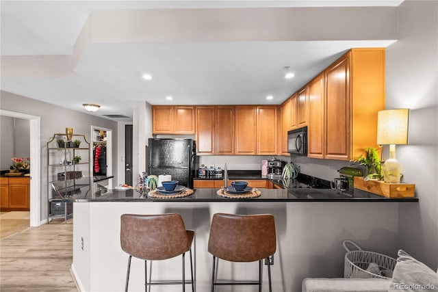 kitchen with dark countertops, recessed lighting, a peninsula, light wood-style floors, and black appliances