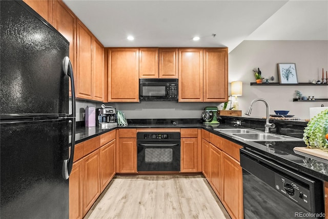 kitchen with dark countertops, black appliances, light wood-type flooring, and a sink