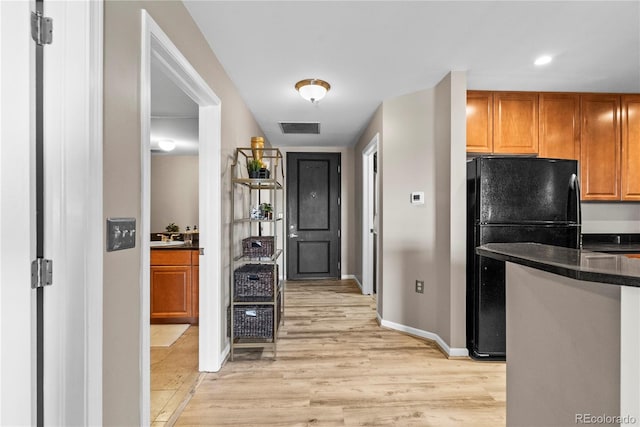 kitchen with dark countertops, visible vents, light wood-style flooring, freestanding refrigerator, and brown cabinetry