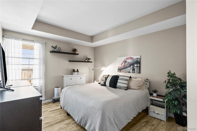 bedroom with a raised ceiling, light wood-style floors, and baseboards