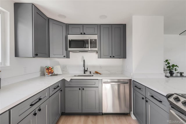 kitchen with sink, gray cabinetry, stainless steel appliances, light stone countertops, and light hardwood / wood-style floors