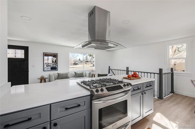 kitchen with stainless steel gas range, gray cabinetry, island range hood, light hardwood / wood-style flooring, and light stone countertops