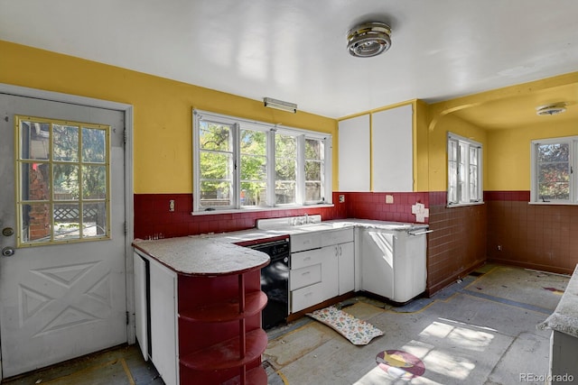 kitchen with dishwasher, tile walls, and white cabinets