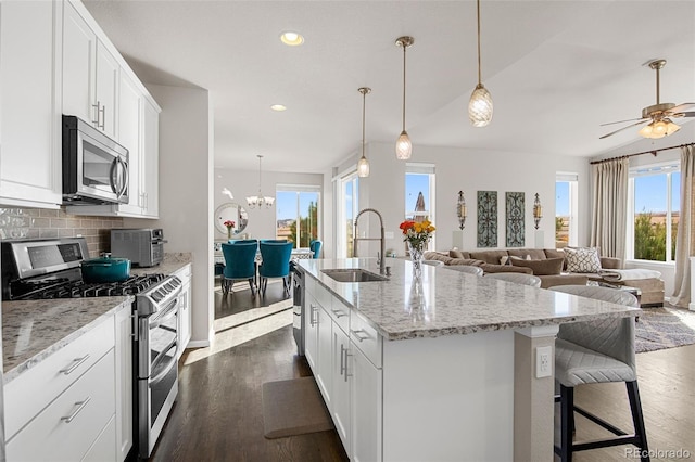 kitchen with stainless steel appliances, sink, white cabinets, an island with sink, and decorative backsplash