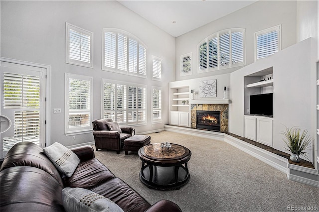 carpeted living room with a high end fireplace, a towering ceiling, built in features, and a wealth of natural light