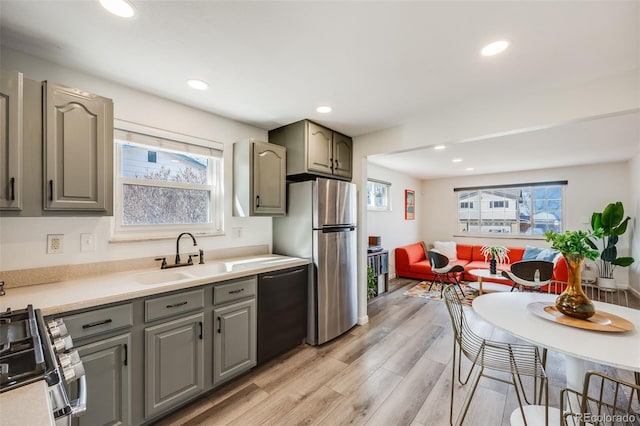 kitchen with gray cabinets, a sink, appliances with stainless steel finishes, light wood finished floors, and a healthy amount of sunlight