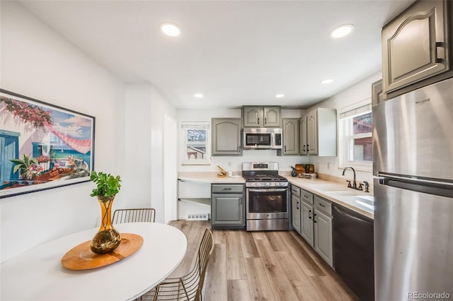 kitchen with light wood finished floors, gray cabinetry, a sink, appliances with stainless steel finishes, and light countertops