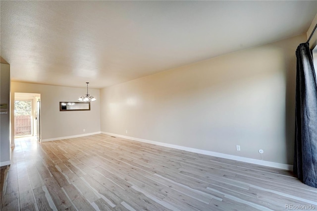 spare room featuring light wood-type flooring and a chandelier