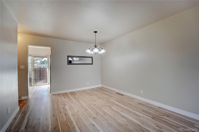 empty room featuring light hardwood / wood-style flooring, a textured ceiling, and a notable chandelier