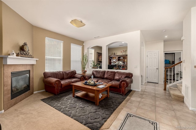 living area featuring light tile patterned floors, arched walkways, visible vents, stairway, and a tiled fireplace