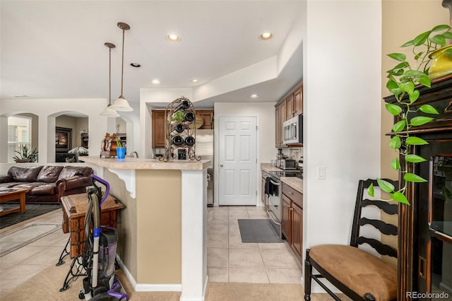 kitchen featuring arched walkways, a breakfast bar area, stainless steel appliances, open floor plan, and light countertops