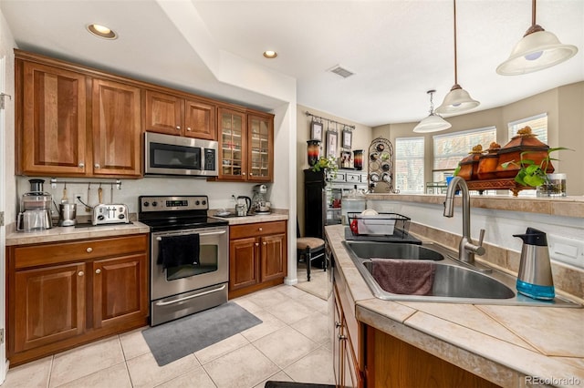 kitchen with stainless steel appliances, light countertops, brown cabinetry, and a sink