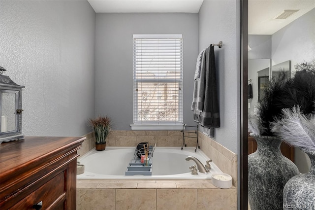 bathroom with visible vents, a textured wall, vanity, and a bath