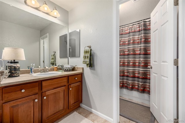 full bath with tile patterned flooring, a textured wall, vanity, and baseboards