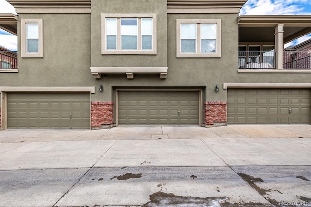 view of front facade featuring driveway, brick siding, an attached garage, and stucco siding