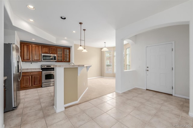 kitchen with appliances with stainless steel finishes, a breakfast bar area, arched walkways, light countertops, and brown cabinetry