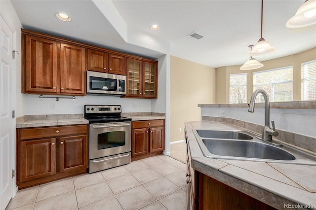 kitchen with appliances with stainless steel finishes, a sink, brown cabinetry, light tile patterned floors, and visible vents