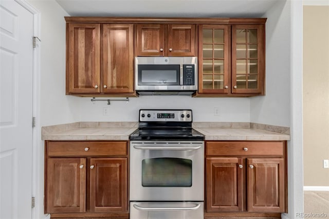 kitchen with glass insert cabinets, brown cabinets, and stainless steel appliances