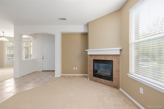 unfurnished living room featuring visible vents, carpet, a tiled fireplace, and a healthy amount of sunlight
