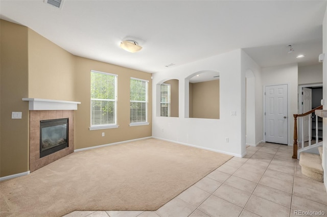 unfurnished living room with visible vents, light carpet, baseboards, stairway, and a tiled fireplace