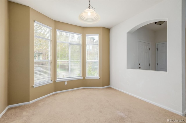 carpeted spare room featuring plenty of natural light, arched walkways, and baseboards