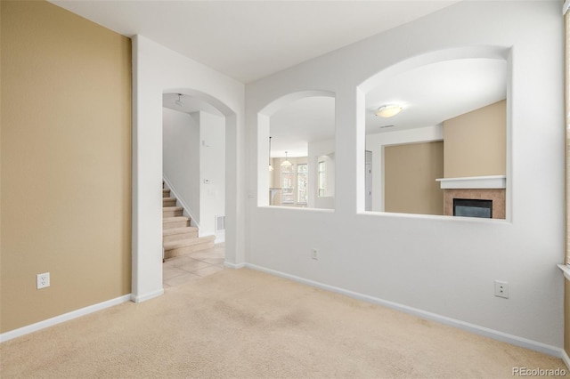empty room featuring carpet floors, baseboards, a glass covered fireplace, and stairway