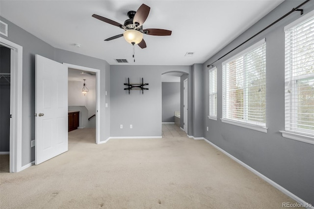 unfurnished bedroom with a closet, visible vents, baseboards, a walk in closet, and arched walkways