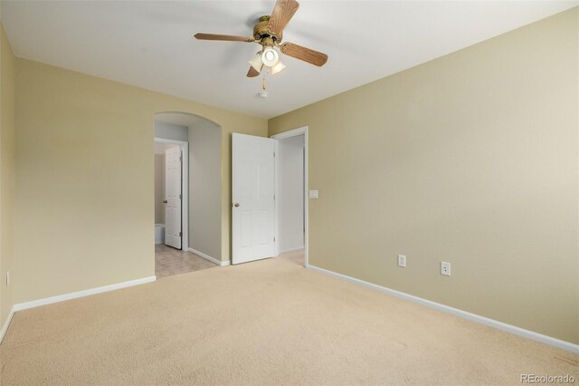 unfurnished bedroom featuring light colored carpet, arched walkways, and baseboards