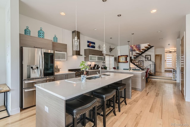 3632 N Pecos St, Denver, CO 80211 - kitchen featuring appliances with stainless steel finishes, modern cabinets, wall chimney range hood, a center island with sink, and light countertops