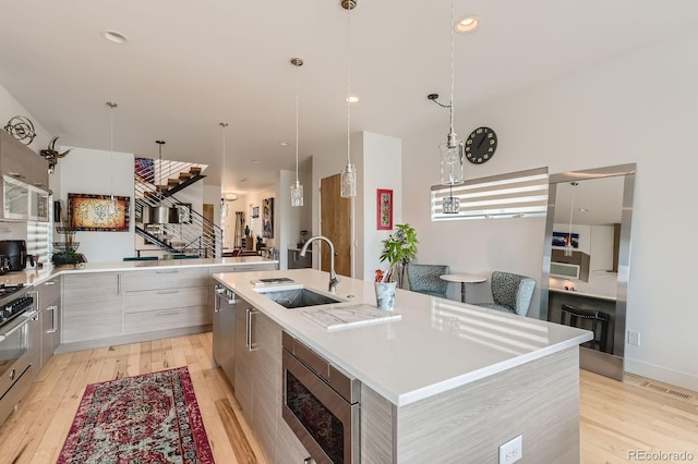 3632 N Pecos St, Denver, CO 80211 - kitchen with modern cabinets, a sink, appliances with stainless steel finishes, a large island with sink, and light wood-style flooring