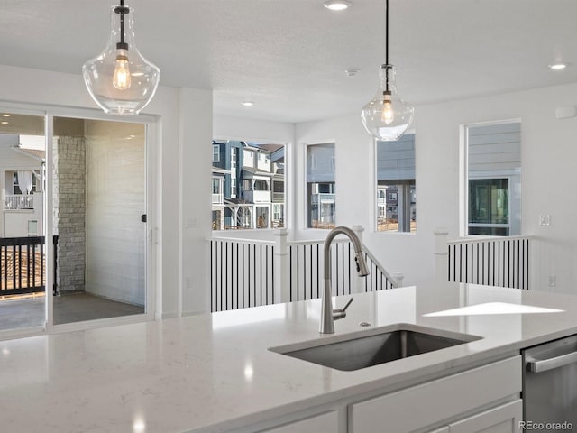kitchen with hanging light fixtures, stainless steel dishwasher, a sink, and light stone countertops