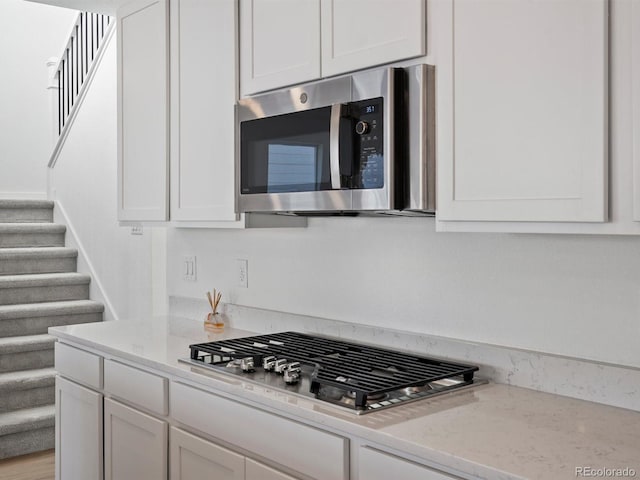 kitchen with appliances with stainless steel finishes, light stone counters, and white cabinets